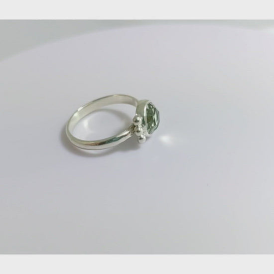 A video of a silver ring with an 8mm round rose cut green amethyst gemstone set in sterling silver. 3 Silver bubble accents aligned along the side.