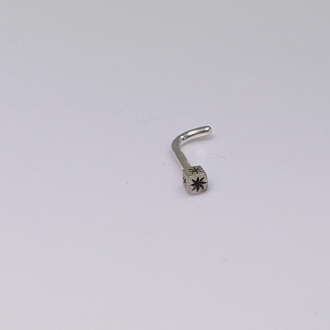 A video of a solid sterling silver cube on a 18g L post nose ring with a hand carved black star on each side.