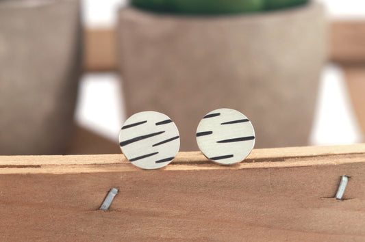 Round silver disc studs with offset black lines randomly spaced.