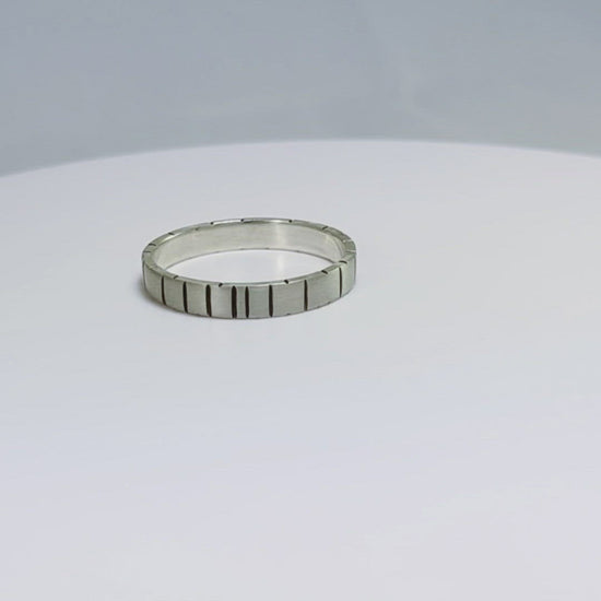 A video of a 4mm silver ring band with randomly spaced black line details.