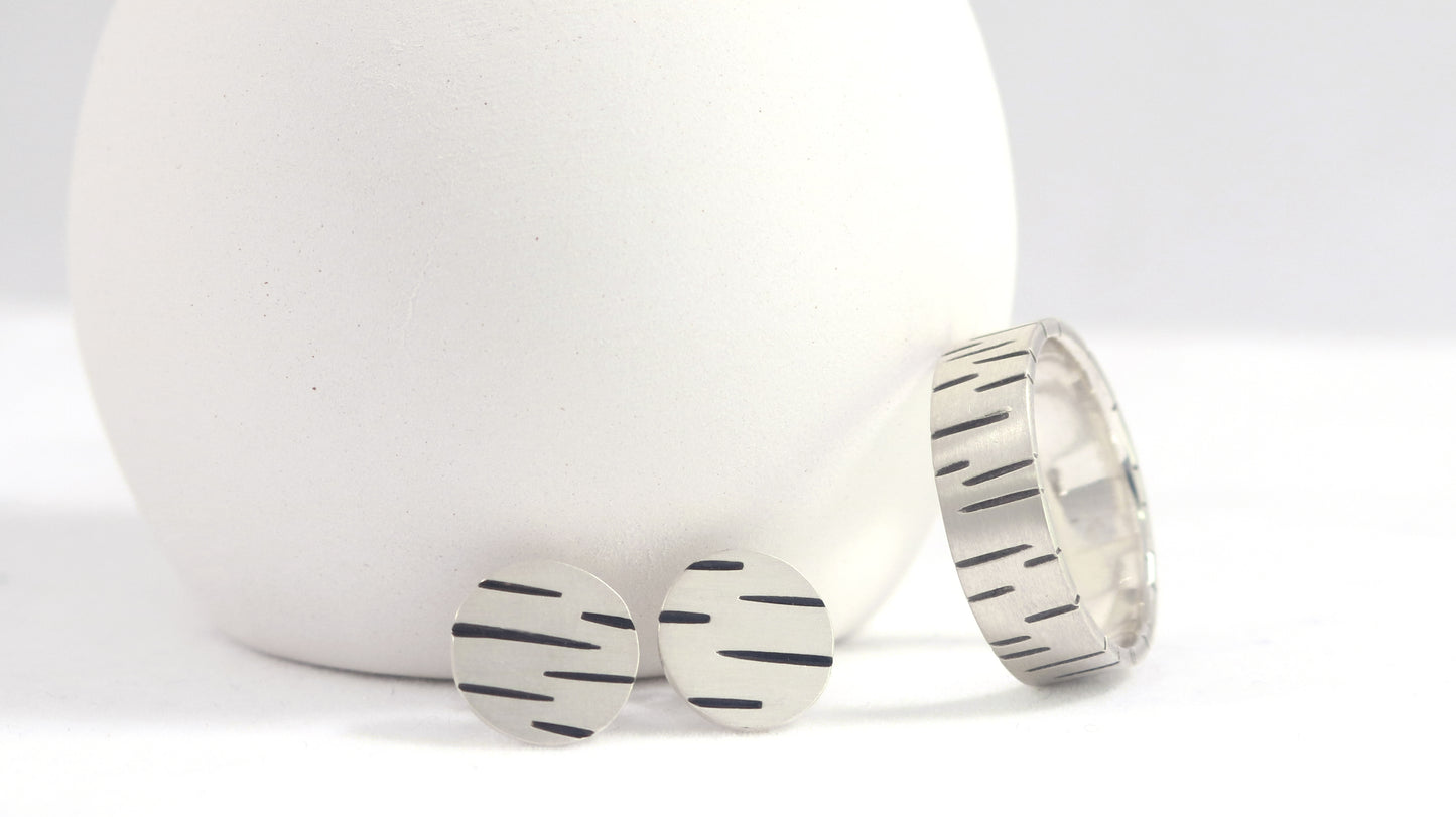 Round silver disc studs with offset black lines randomly spaced alongside a matching ring.