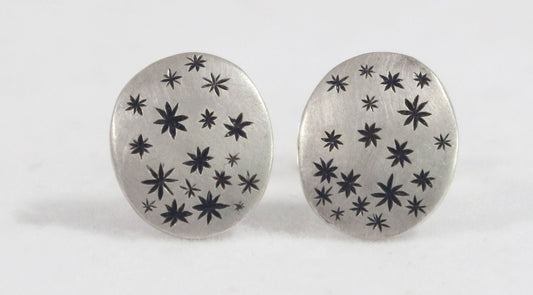 A pair of domed oval sterling silver studs covered in hand carved, black stars. 