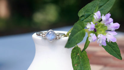 Natural cushion cut rainbow moonstone set in sterling silver with 2 silver bubble pyramid accents on a sterling silver ring band.