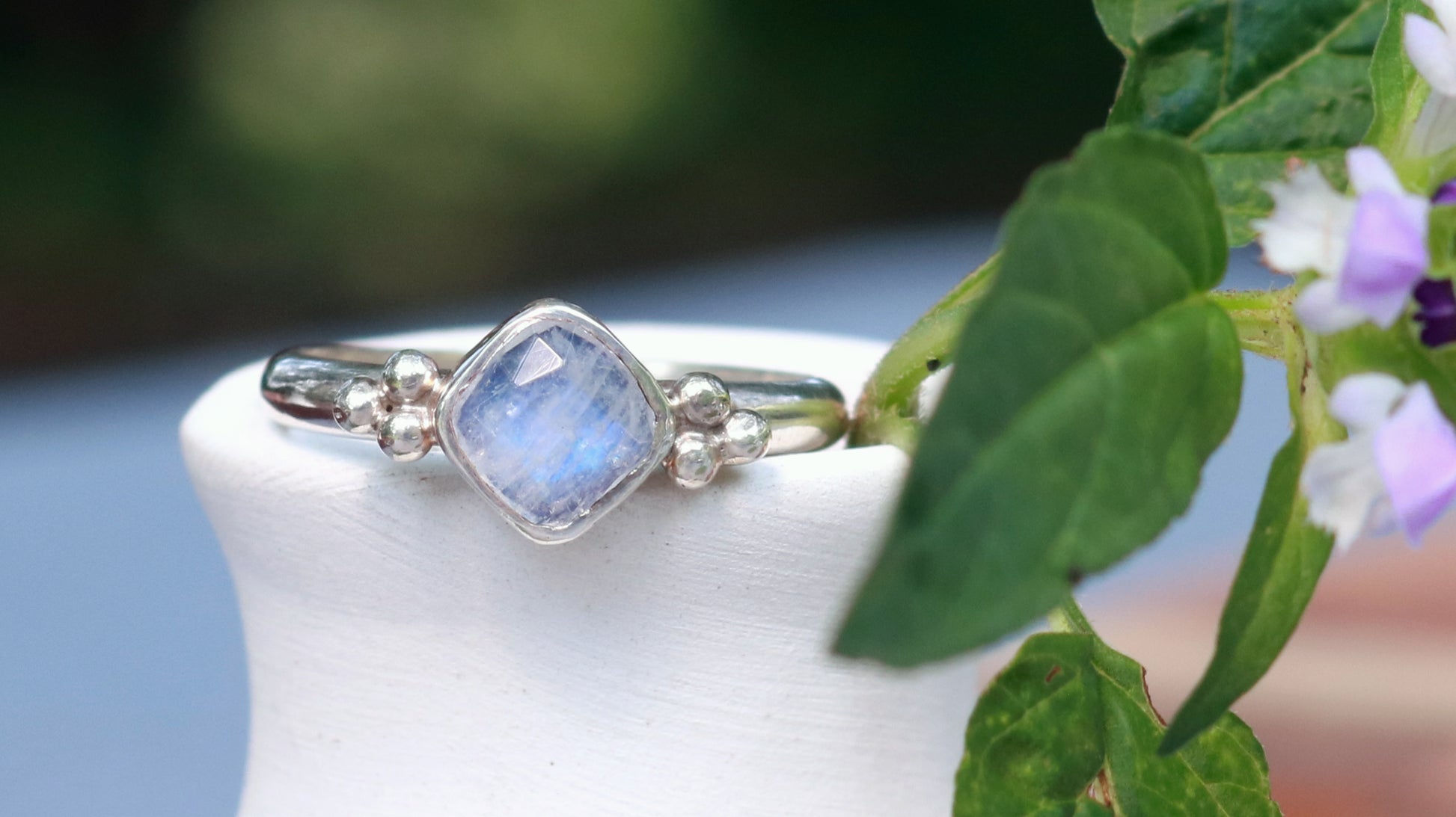 Natural cushion cut rainbow moonstone set in sterling silver with 2 silver bubble pyramid accents on a sterling silver ring band.