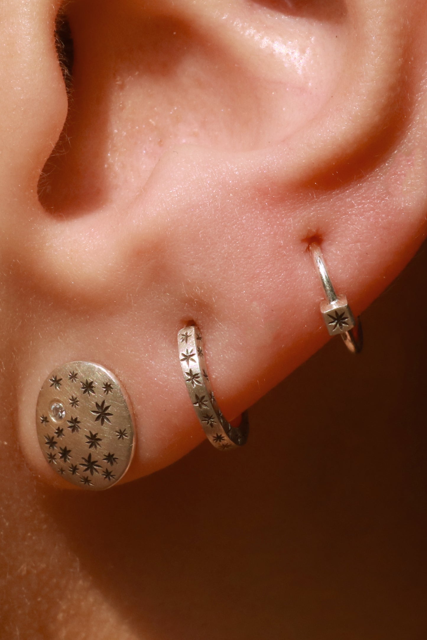 A model wearing hoops made from 1.5mm x 1.5mm square sterling silver, hand cut black stars on all outward facing sides. 