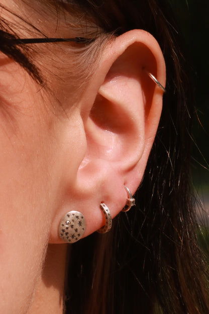 A model wearing hoops made from 1.5mm x 1.5mm square sterling silver, hand cut black stars on all outward facing sides. 