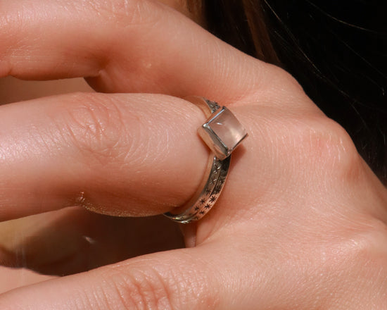 A sterling silver ring with a square rose quartz gemstone set in the center diagonally. Black stars going down each side of the ring band.