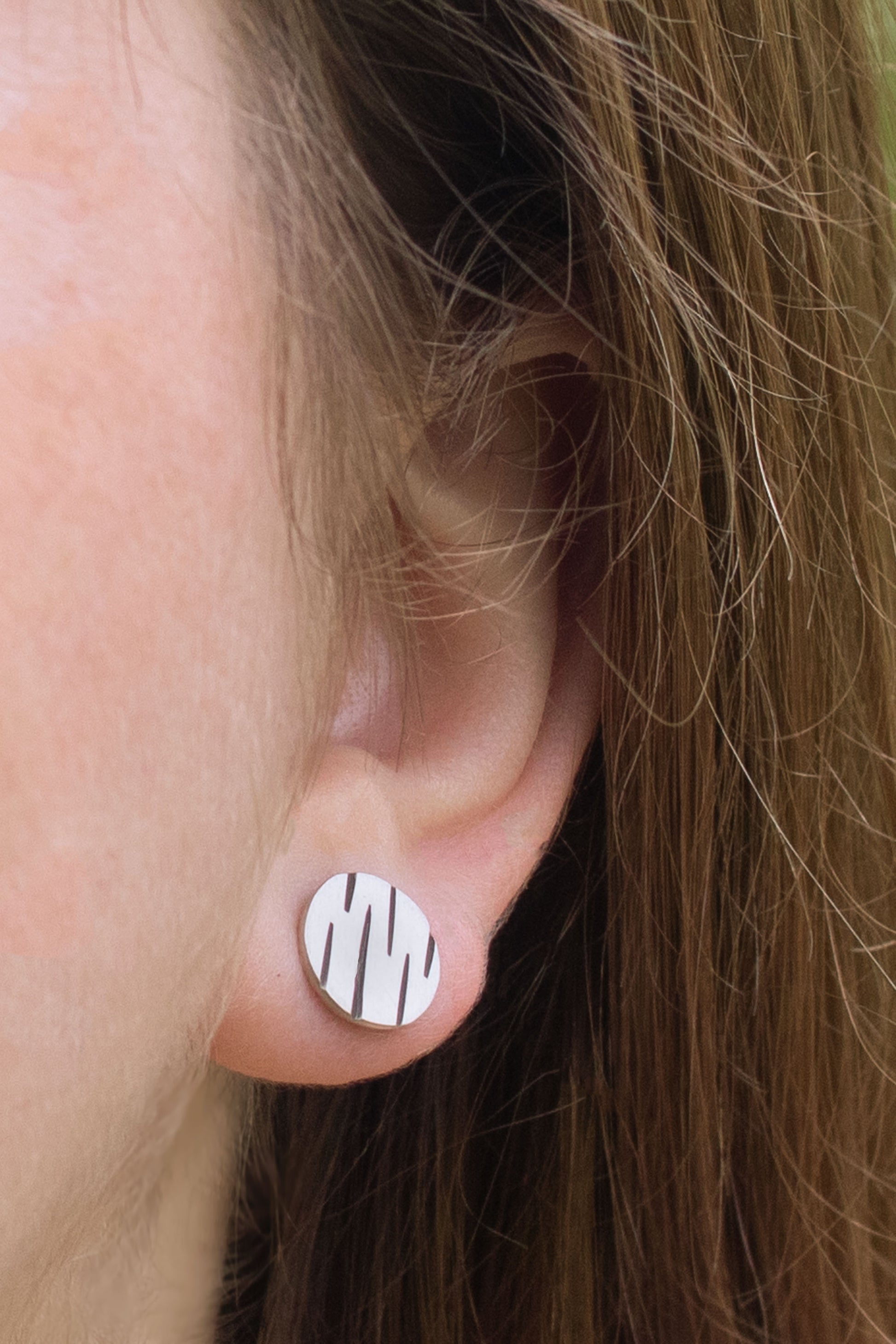 A model wearing round silver disc studs with offset black lines randomly spaced.