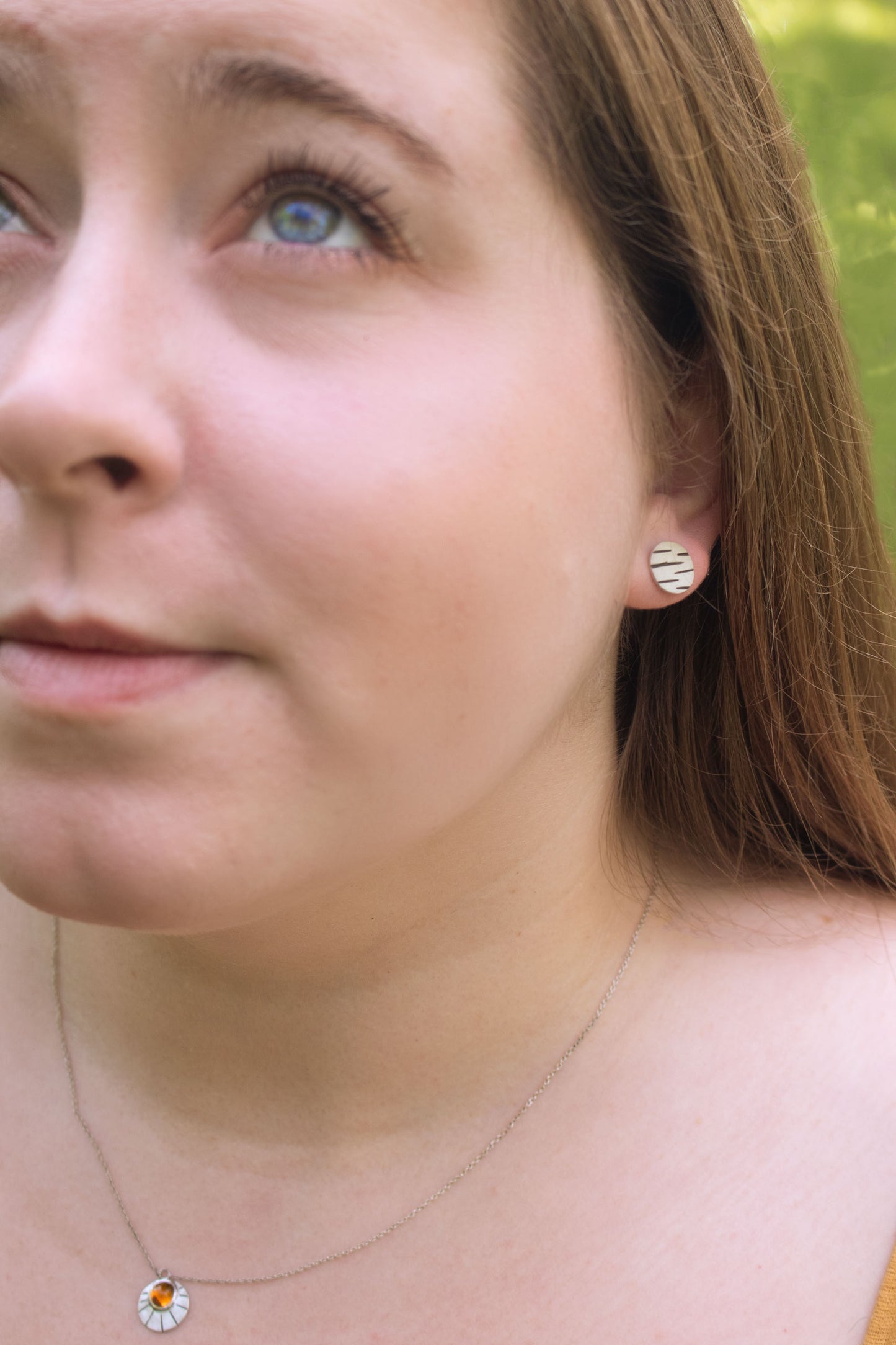 A model wearing round silver disc studs with offset black lines randomly spaced.