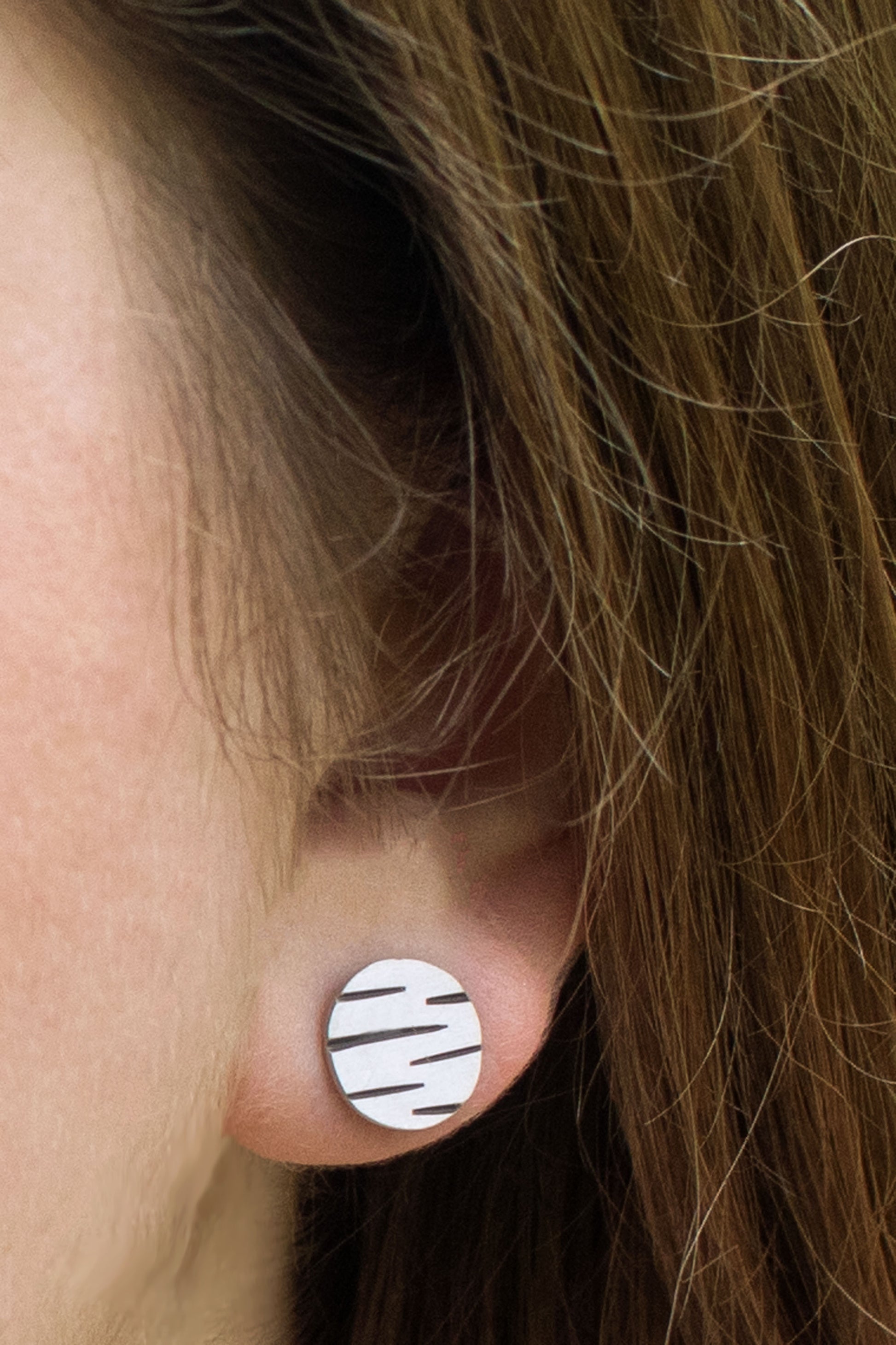 A model wearing round silver disc studs with offset black lines randomly spaced.