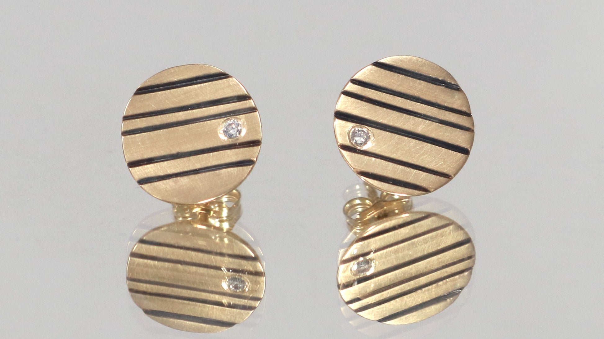 Round 14k gold disc studs with black lines randomly spaced and a single white diamond flush set at the edge.