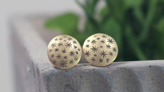 A pair of 14k yellow gold earrings that are 2 domed circles adorned with hand carved black stars.