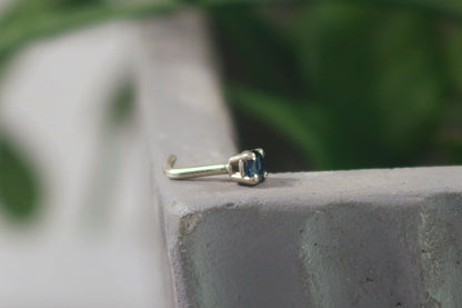 The side view of a basket set faceted blue sapphire nose stud made from 14k white gold.