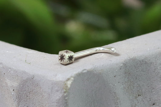 A solid sterling silver cube on a 18g L post nose ring with a hand carved black star on each side.