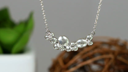 A curved cluster of silver bubbles of different sizes on a sterling silver chain.