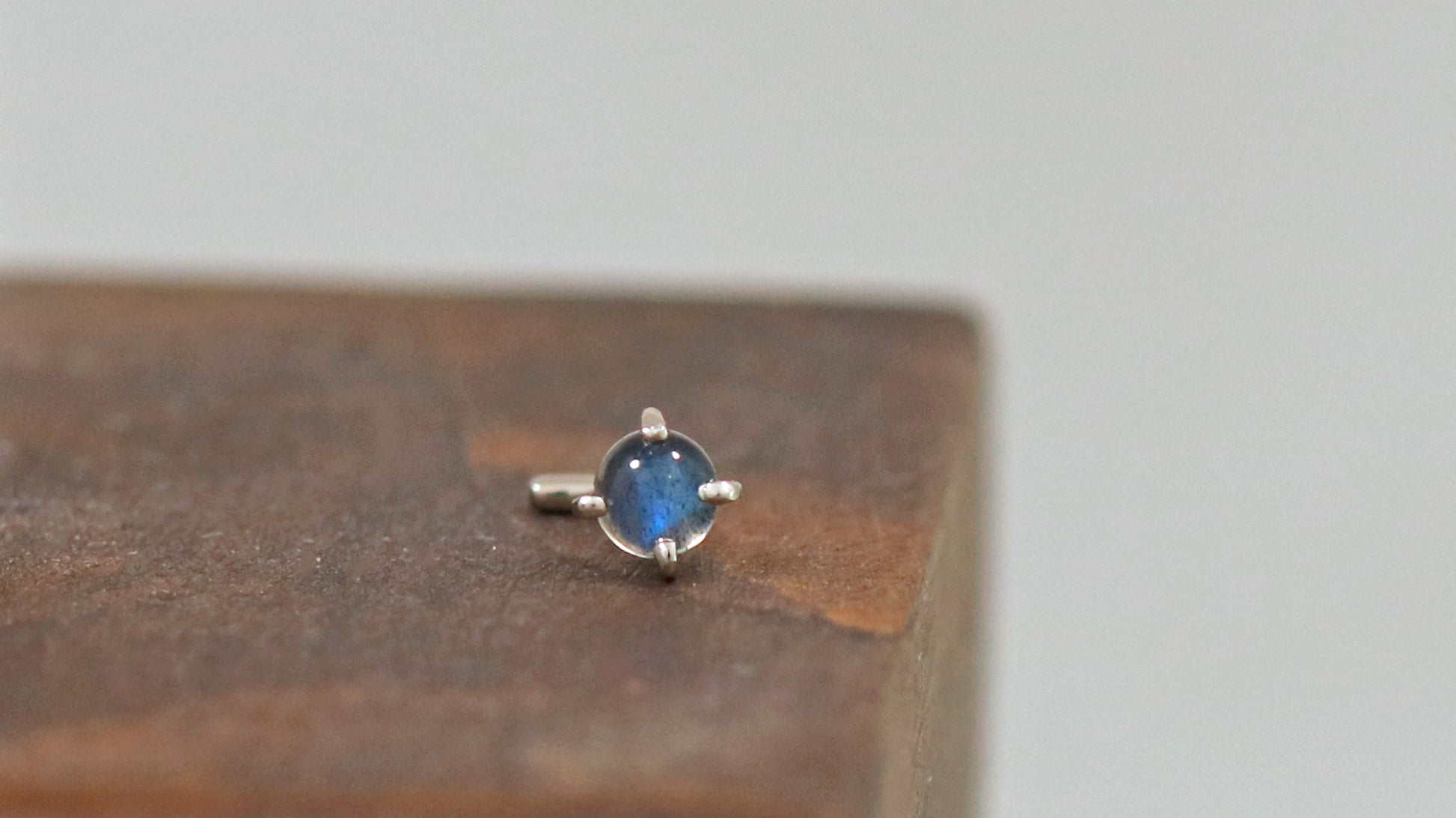 A 14k white gold nose stud with a round rainbow moonstone, set in prongs.