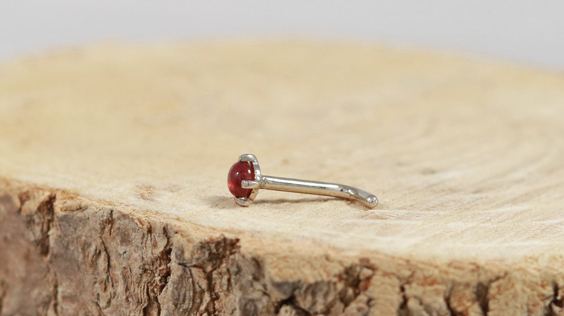 The side view of a 14k white gold nose stud with a round ruby set with prongs.