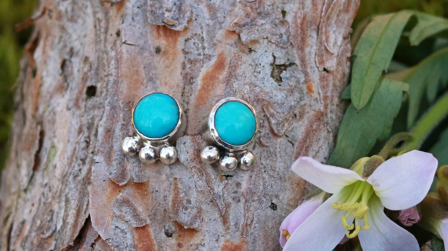 A pair of 5mm, round turquoise stones set in sterling silver with three silver bubbles aligned along the bezel.