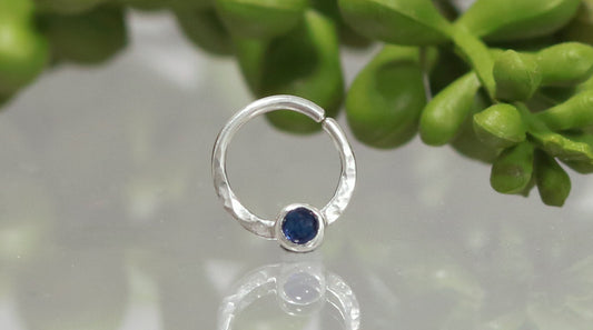 A sterling silver hoop, flattened and textured at the bottom, with a blue sapphire set in a bezel on top of the textured flat section.