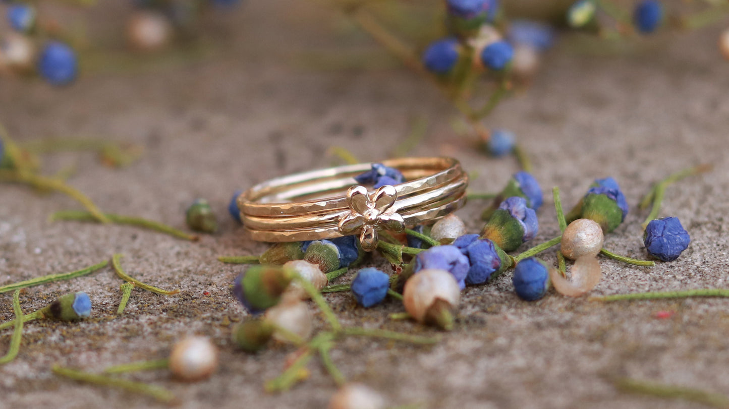 Thin yellow gold stacking rings with a hammer texture and a yellow gold flower stacking ring.