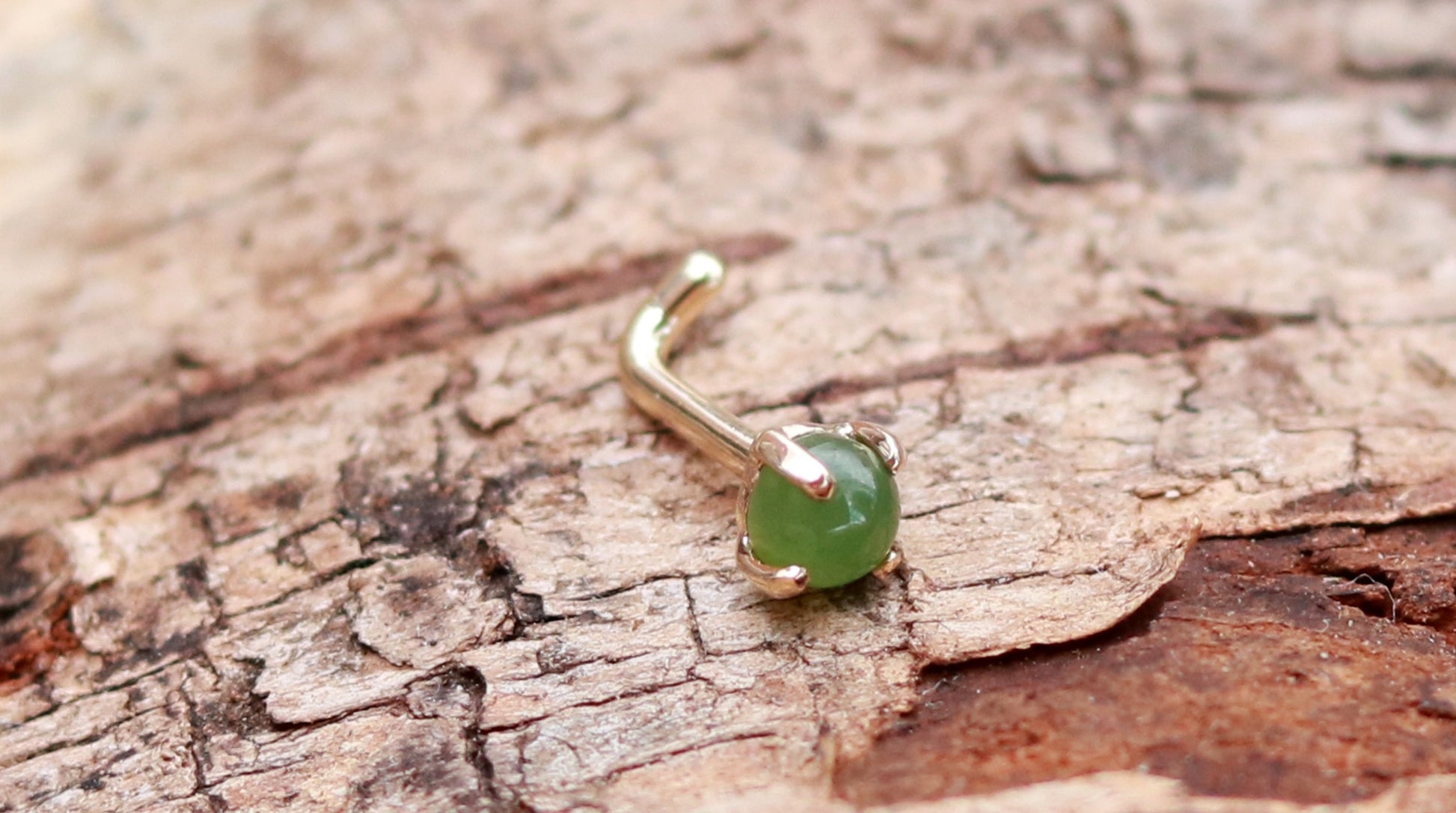 A 14k yellow gold nose stud with a round jade, set in prongs.