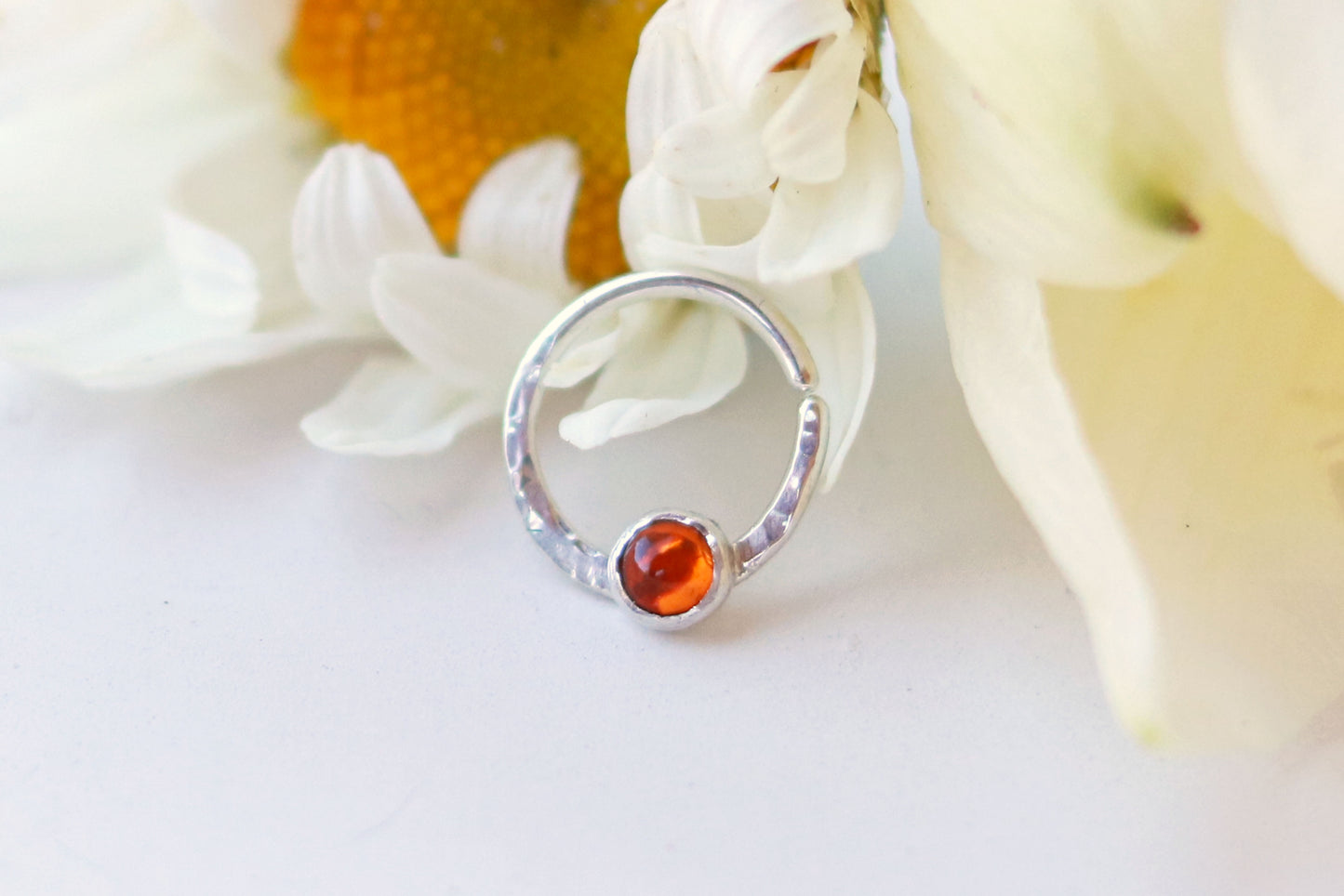 A sterling silver hoop, flattened and textured at the bottom, with an amber set in a bezel on top of the textured flat section.