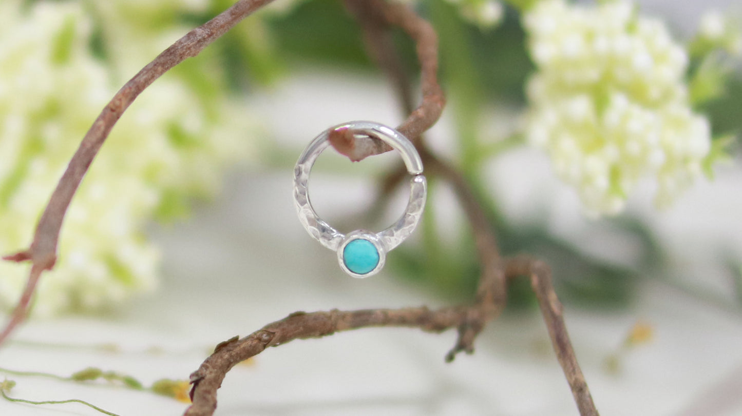 A sterling silver hoop, flattened and textured at the bottom, with a turquoise set in a bezel on top of the textured flat section.