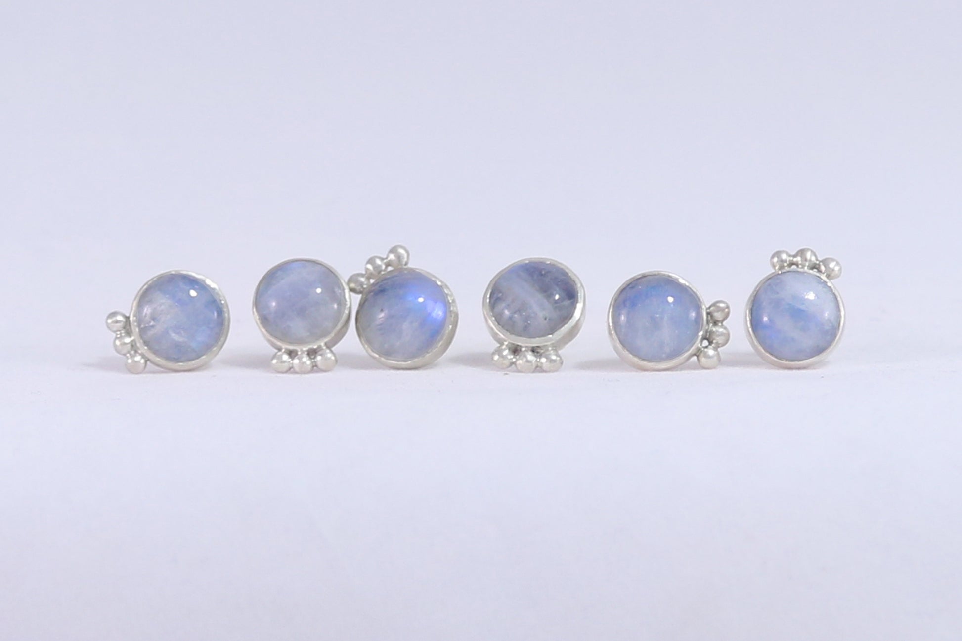 Three pairs of round rainbow moonstone stud earrings with 3 silver bubbles in a row at the bottom. 