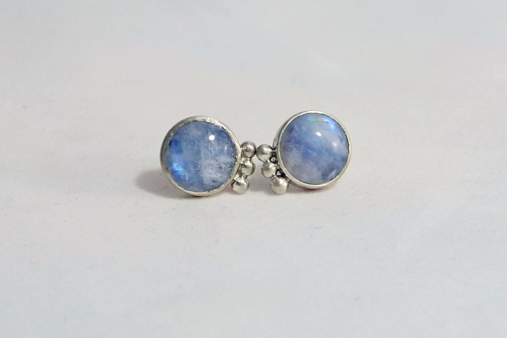 A pair of round rainbow moonstone stud earrings with 3 silver bubbles in a row on the sides. 