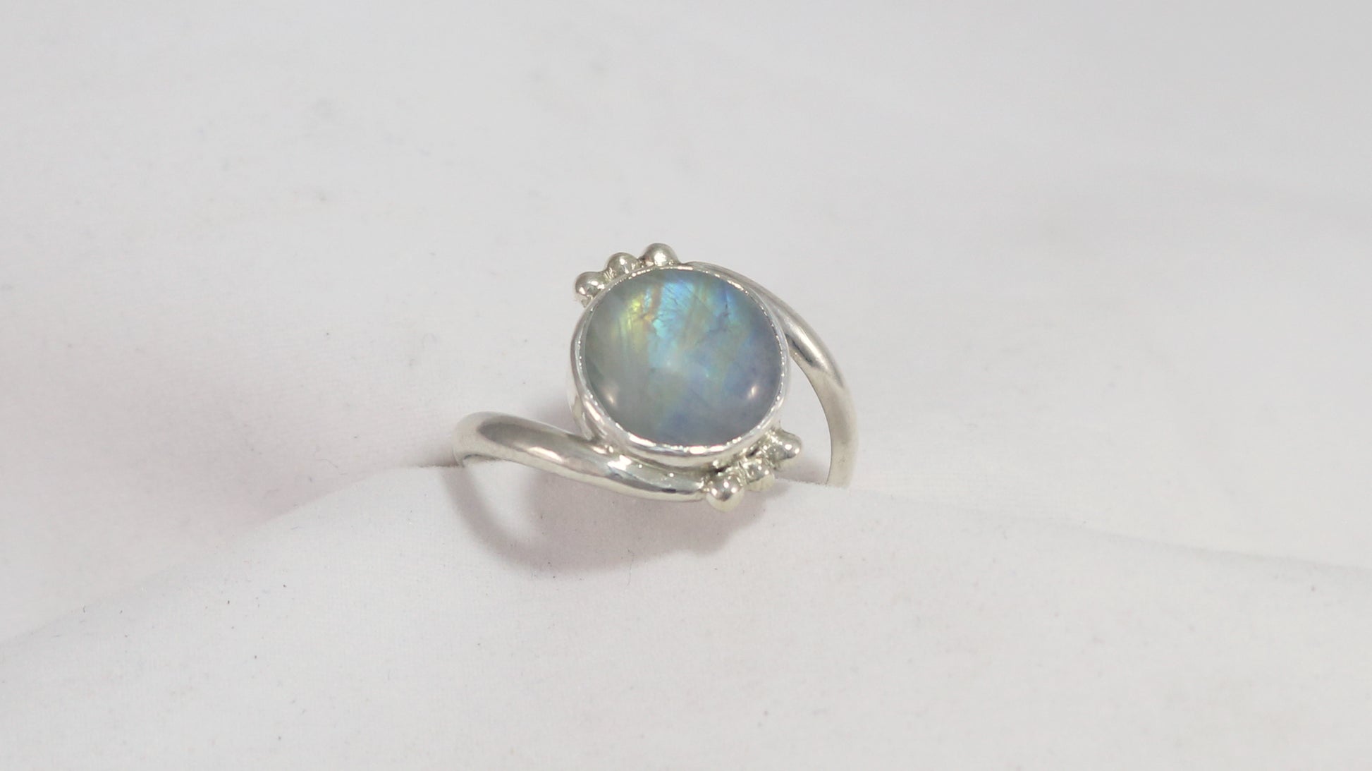 Round natural rainbow moonstone set in sterling silver bezel on a bypass ring band with silver bubble accents. 