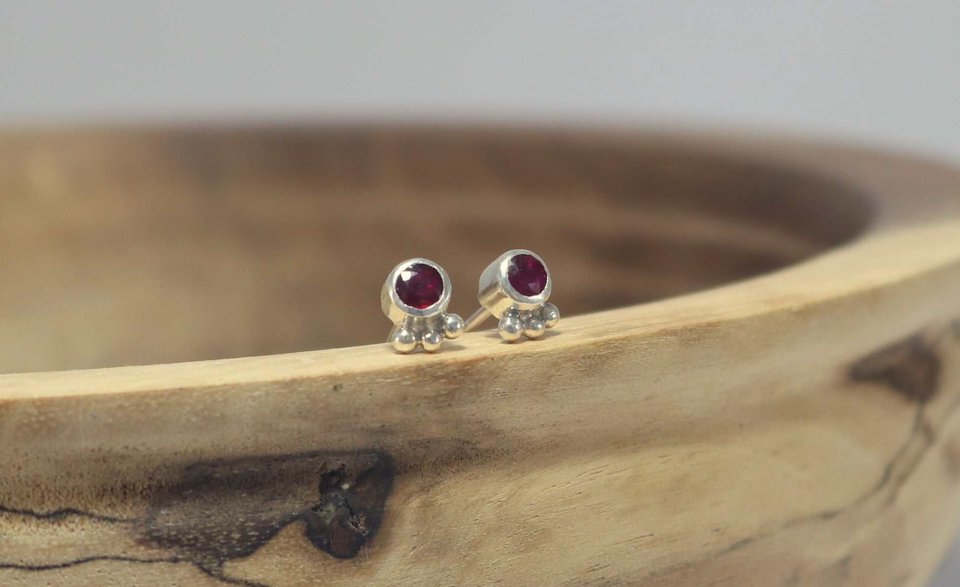 A pair of deep pink, round, faceted rhodolites set in sterling silver bezels with three silver bubbles aligned along the bezel.