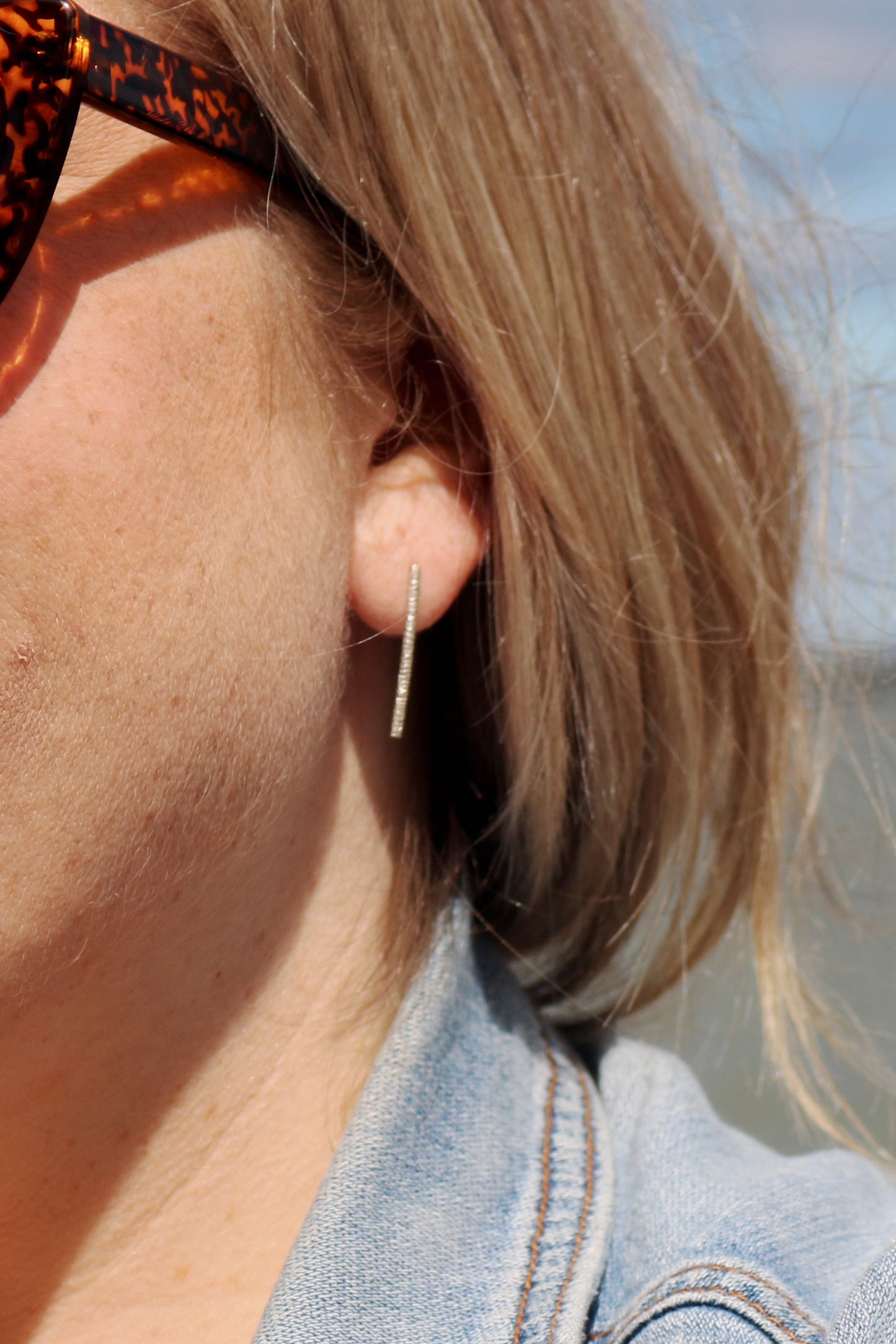 A model wearing sterling silver long bar studs with linear texture.