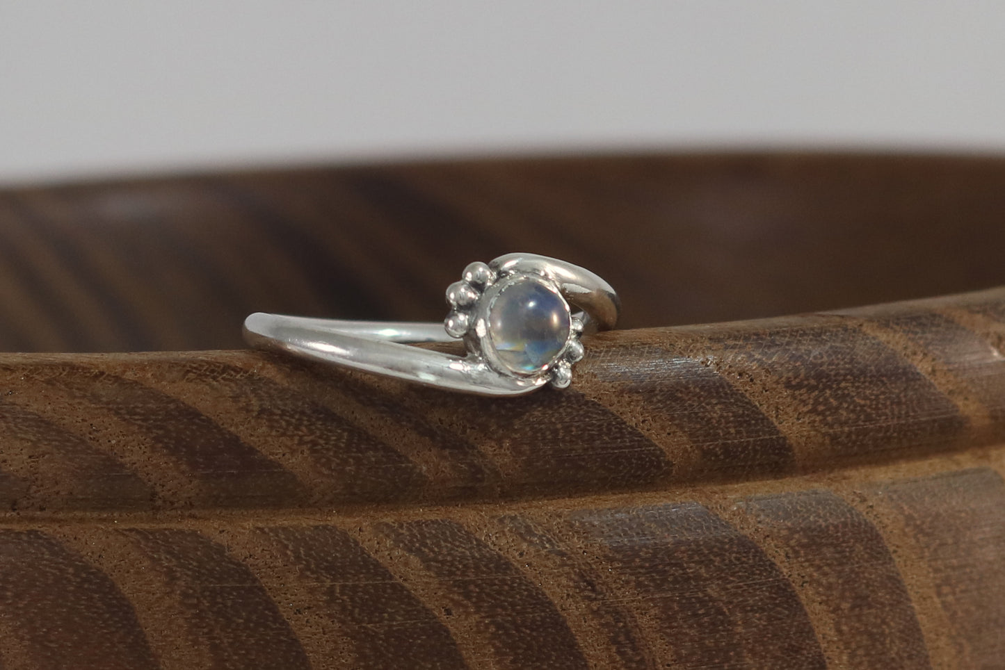 Round natural rainbow moonstone set in sterling silver bezel on a bypass ring band with silver bubble accents. 