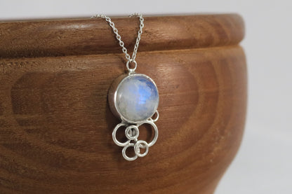 Natural round rainbow moonstone on a silver chain, with 6 silver open circles placed below to look like a cluster of bubbles.