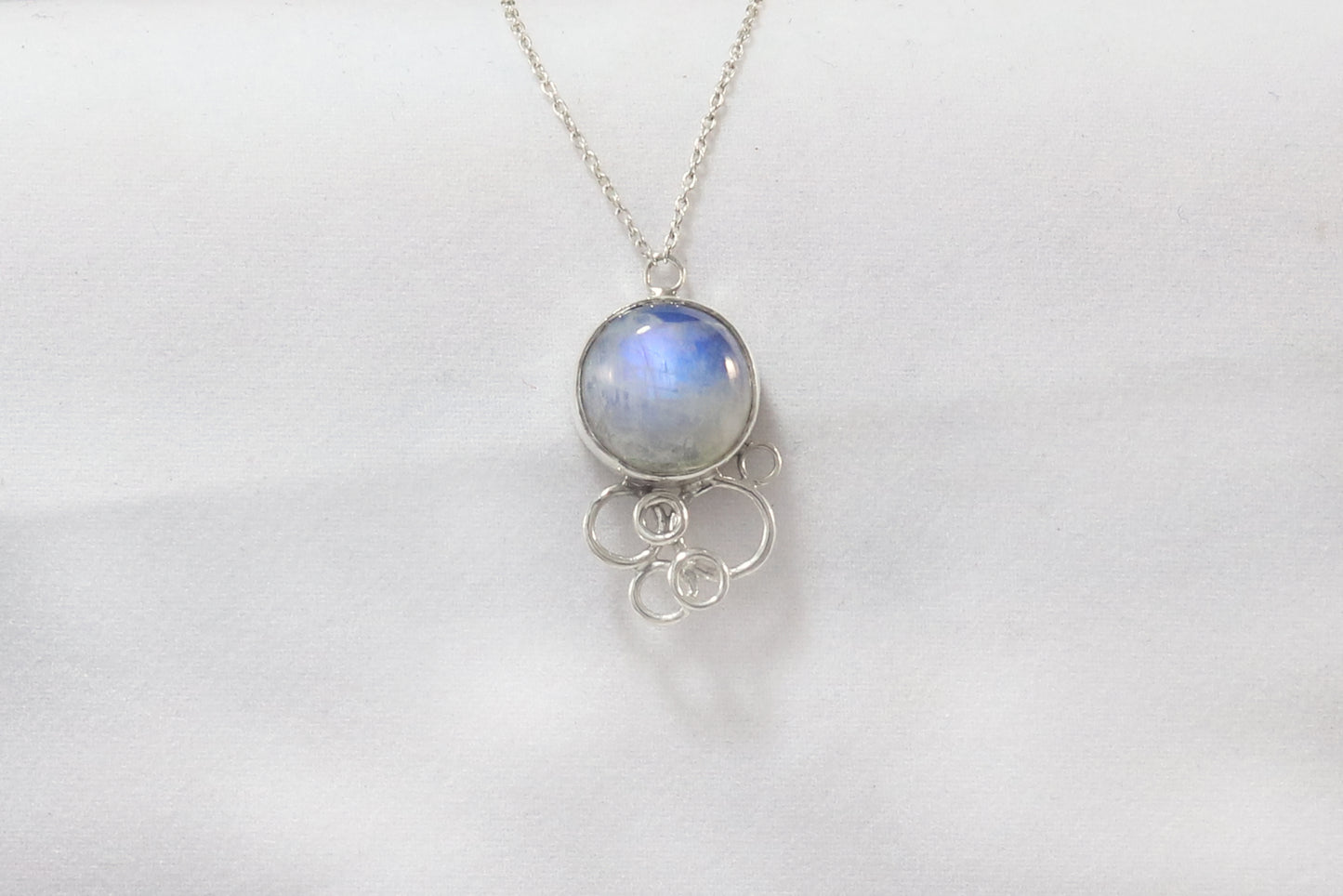 Natural round rainbow moonstone on a silver chain, with 6 silver open circles placed below to look like a cluster of bubbles.