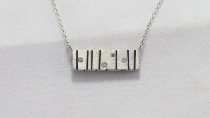 A large sterling silver bar with randomly spaced black lines and 4 white flush set diamonds.