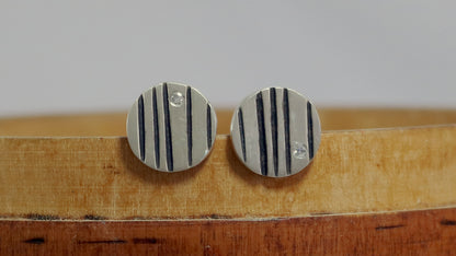 Round silver disc studs with black lines randomly spaced and a single white diamond flush set at the edge.