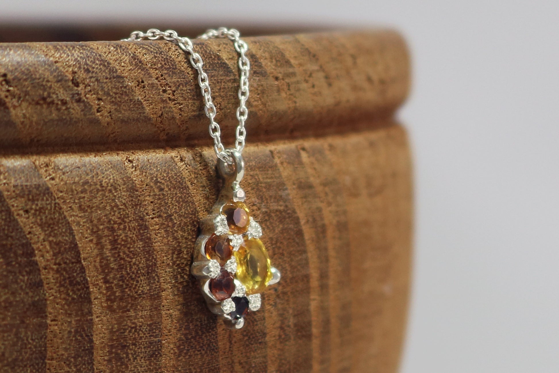 A sterling silver cluster pendant of natural gemstones in a yellow to red gradient on a sterling silver chain.
