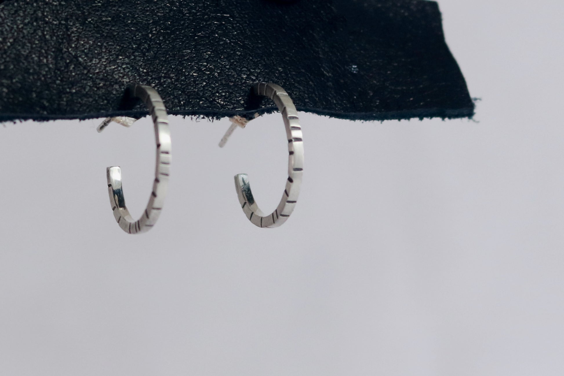 Thin sterling silver hoop earrings with randomly spaced black lines on each side. .