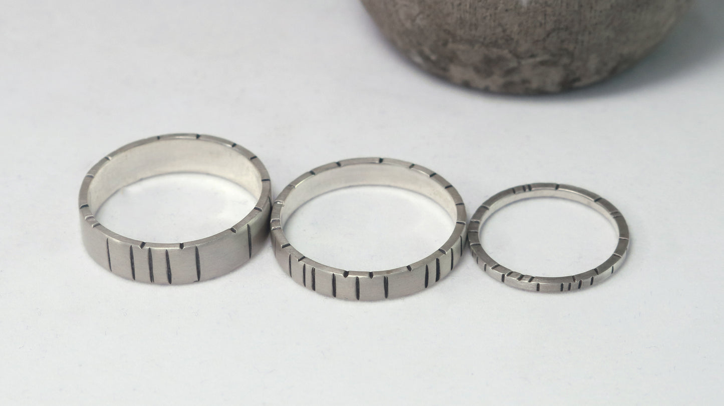 A 4mm silver ring band with randomly spaced black line details.