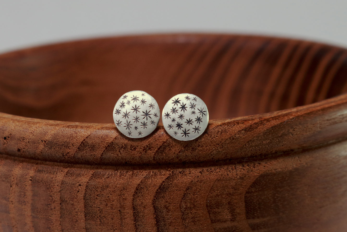 A pair of round, domed, silver, stud earrings with hand carved black stars.