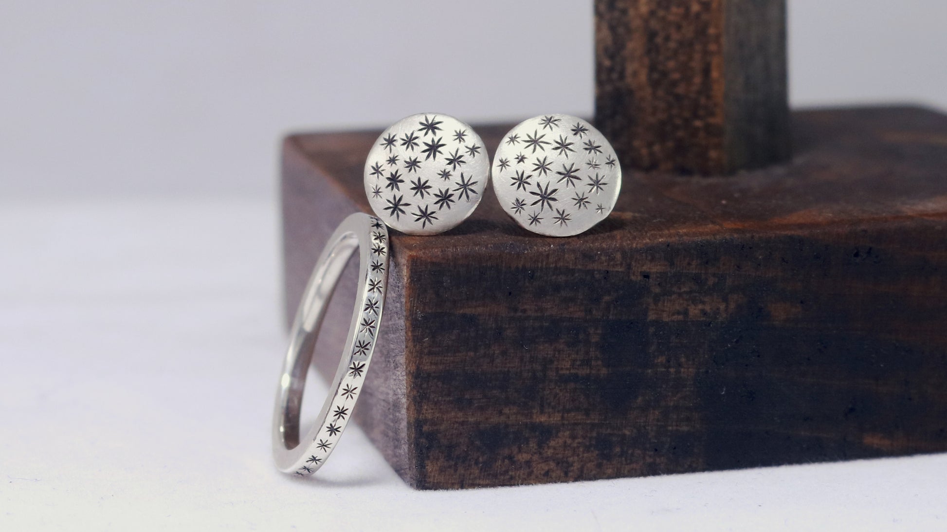A pair of round, domed, silver, stud earrings with hand carved black stars photographed with a star ring.