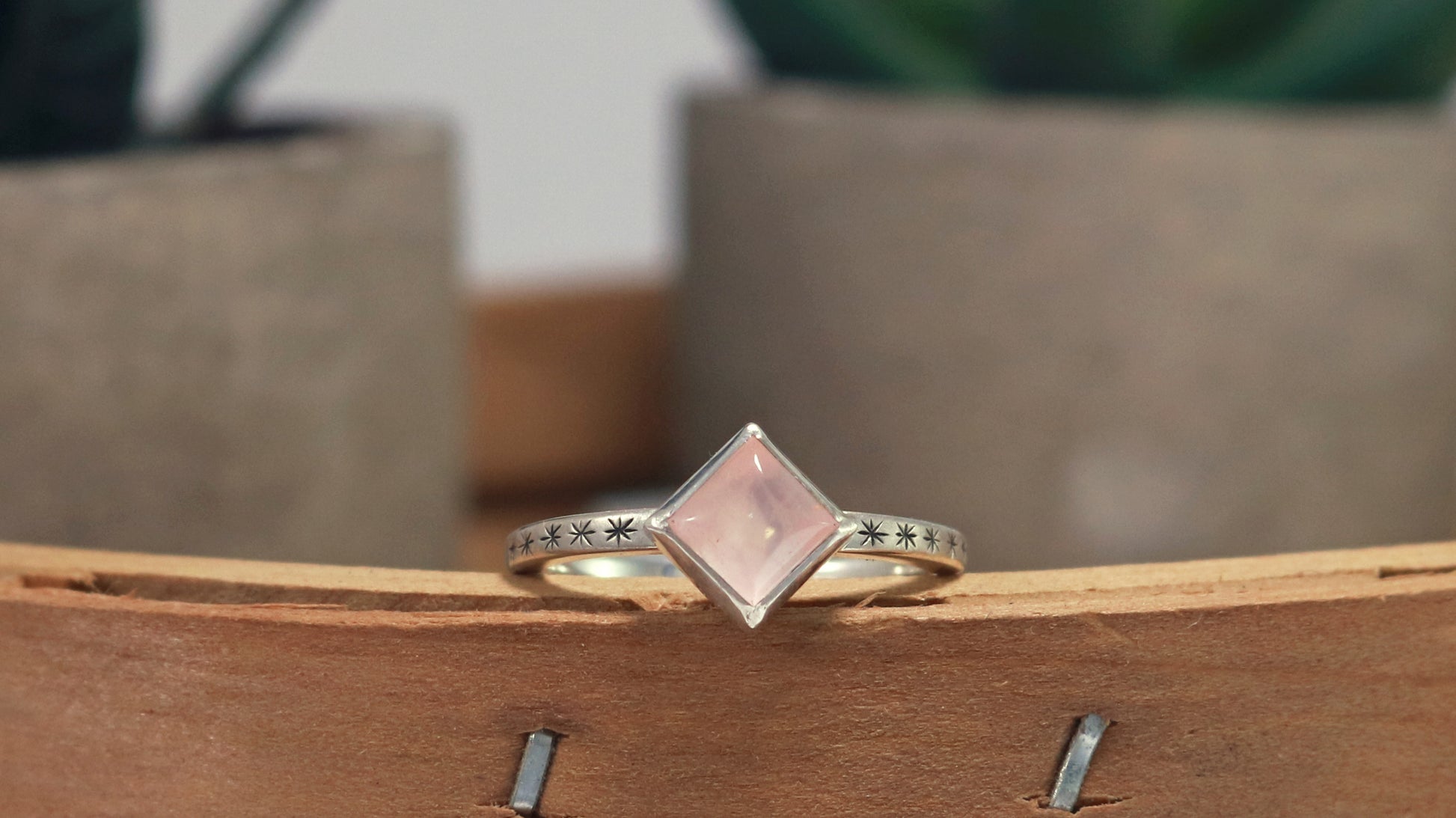 A sterling silver ring with a square rose quartz gemstone set in the center diagonally. Black stars going down each side of the ring band.