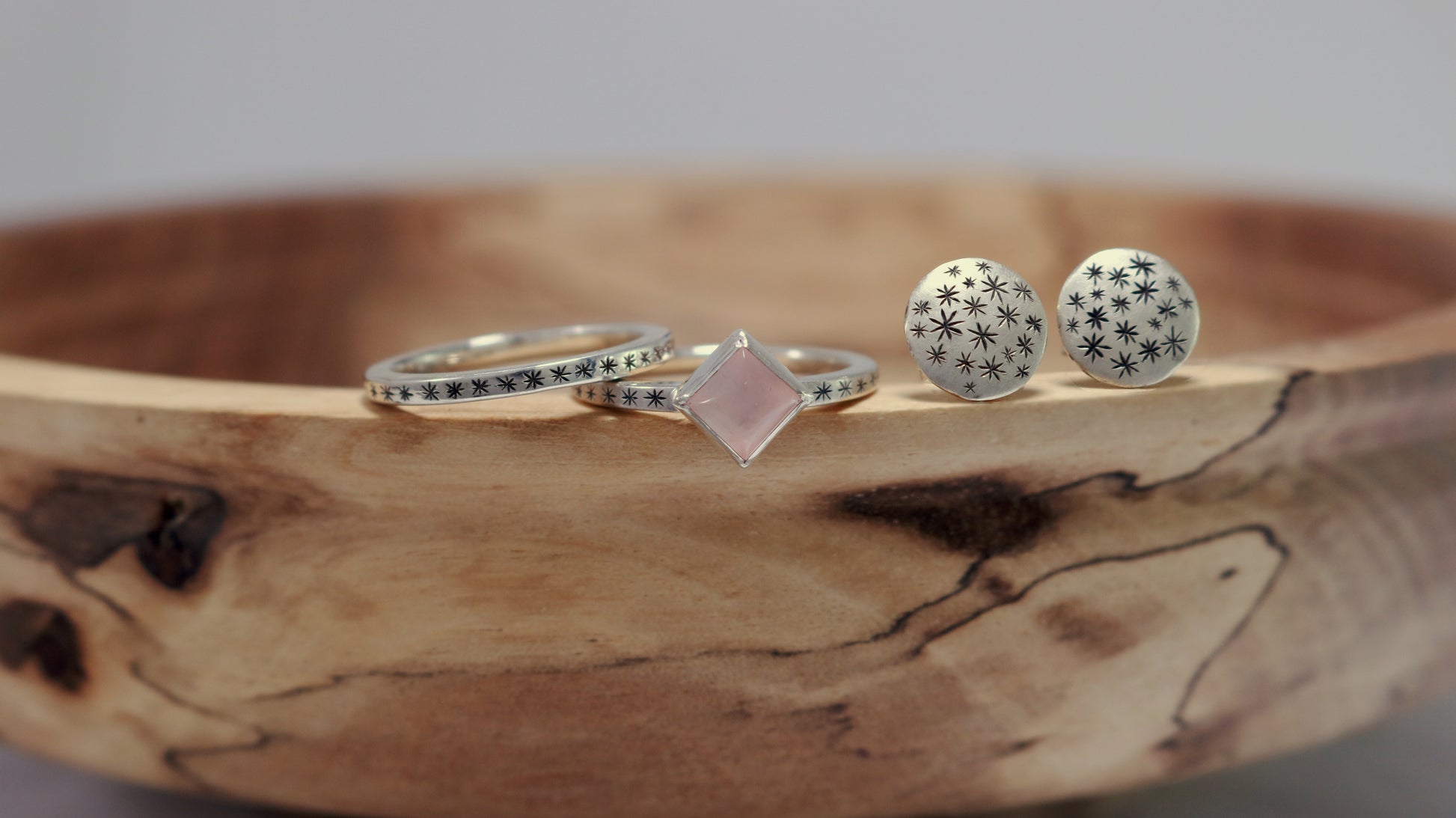 A sterling silver ring with a square rose quartz gemstone set in the center diagonally. Black stars going down each side of the ring band.