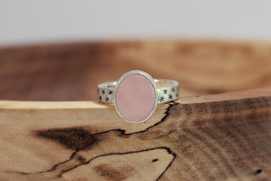 Oval natural gemstone set in sterling silver bezel on a wide sterling silver ring band with checker board of hand cut black stars on either side.