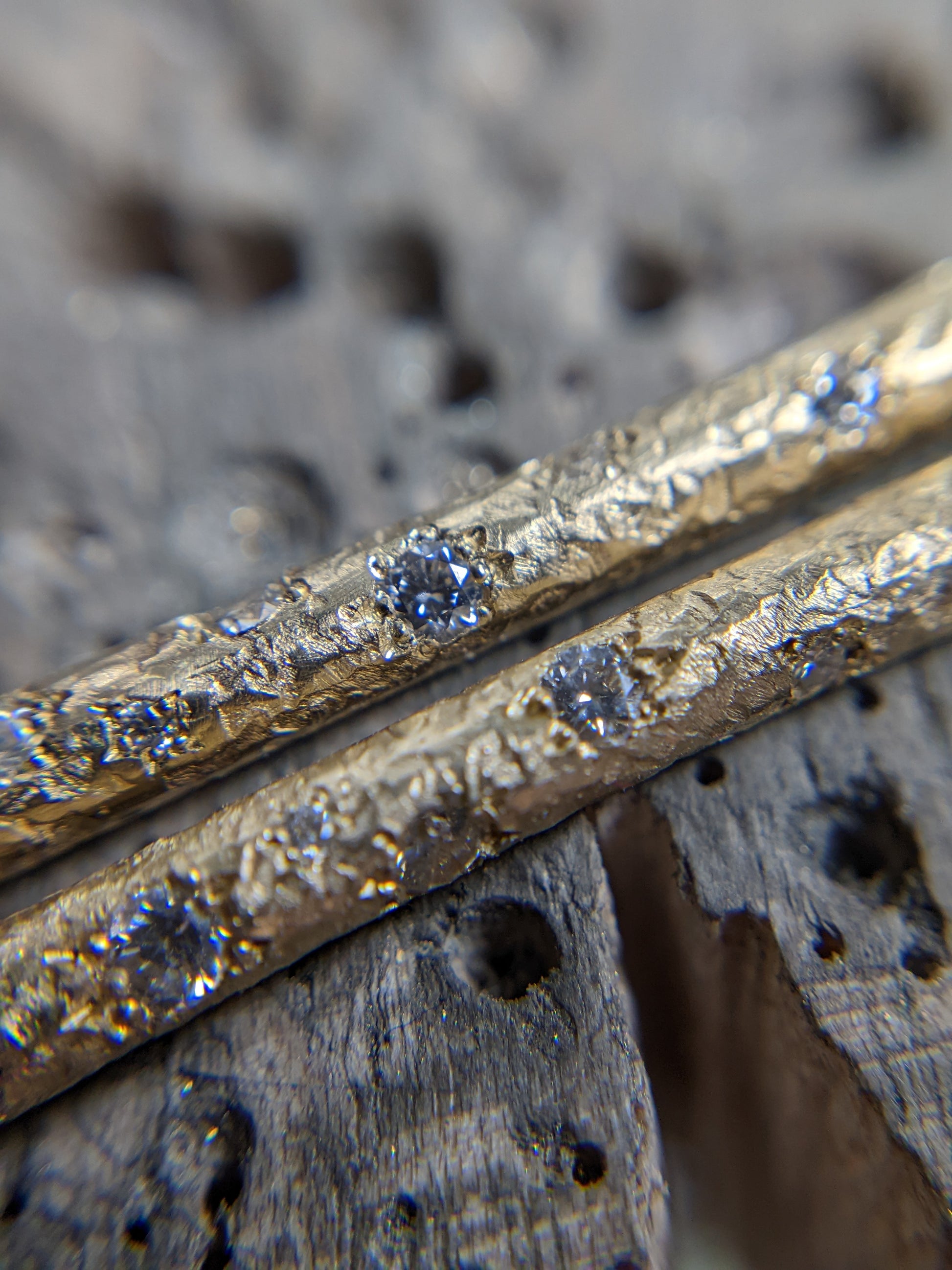 A  close up of a solid 14k yellow gold textured bar with 10 diamonds of various sizes cascading down the bar.