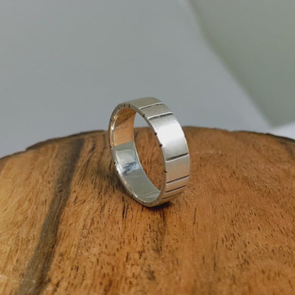 A video of a 6mm thick silver ring band with randomly spaced black line details.