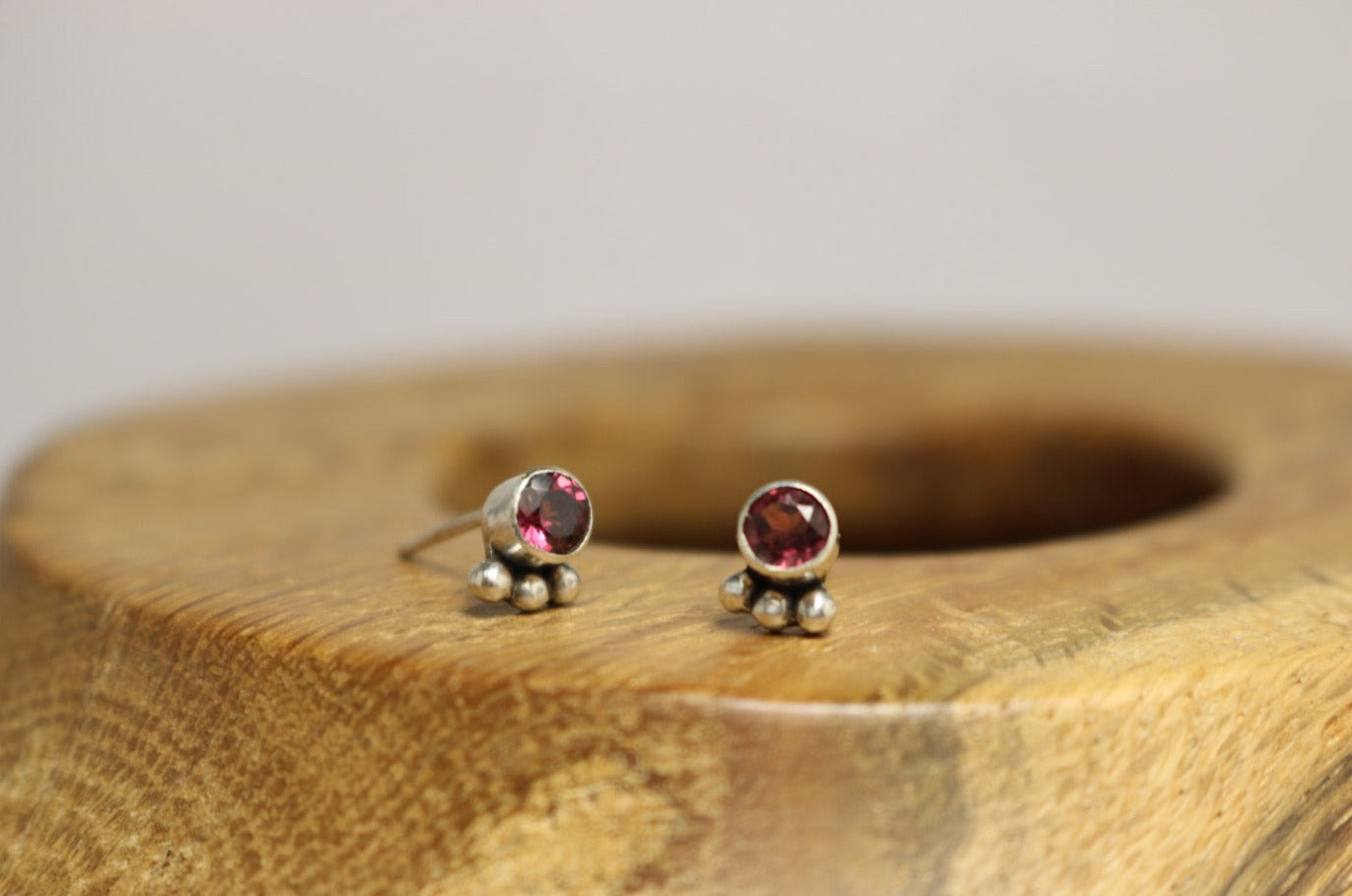 A pair of deep pink, round, faceted rhodolites set in sterling silver bezels with three silver bubbles aligned along the bezel.
